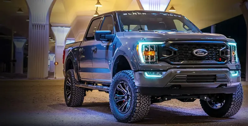 Gray Ford F-150 Black Widow lifted truck with LED lighting, parked at night